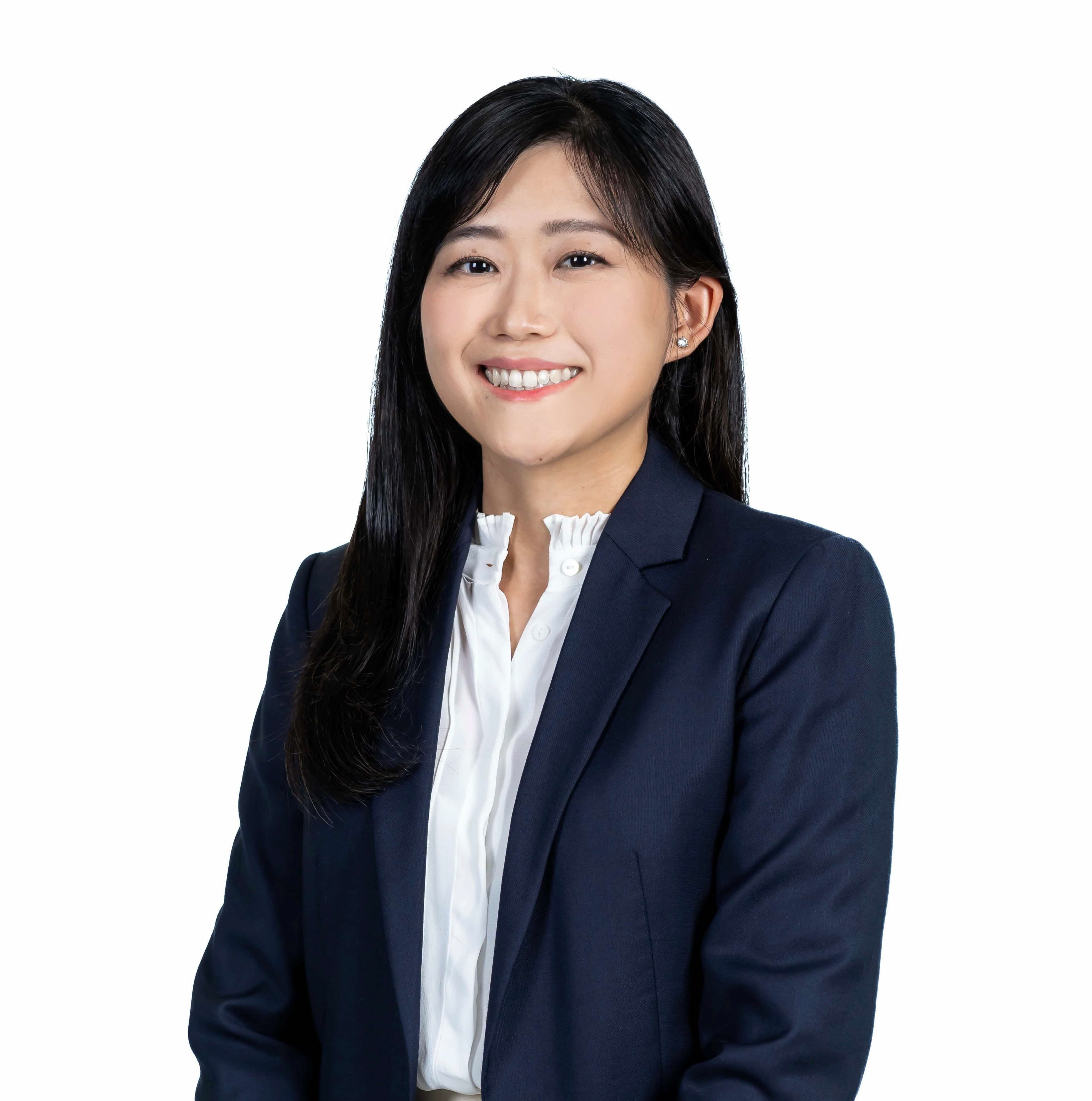 A smiling young woman with long black hair wearing a navy blazer and white ruffled blouse on a white background.